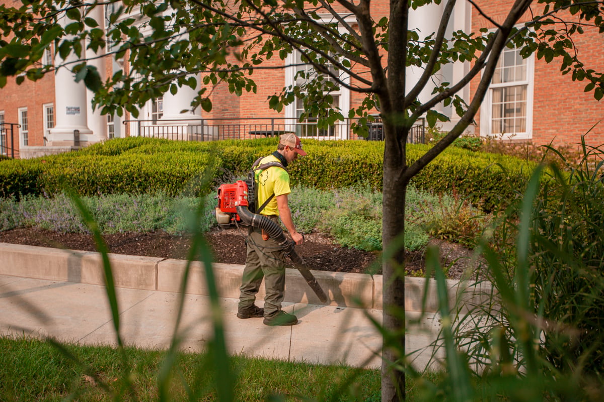 Grounds crew clearing beds along a brick campus building