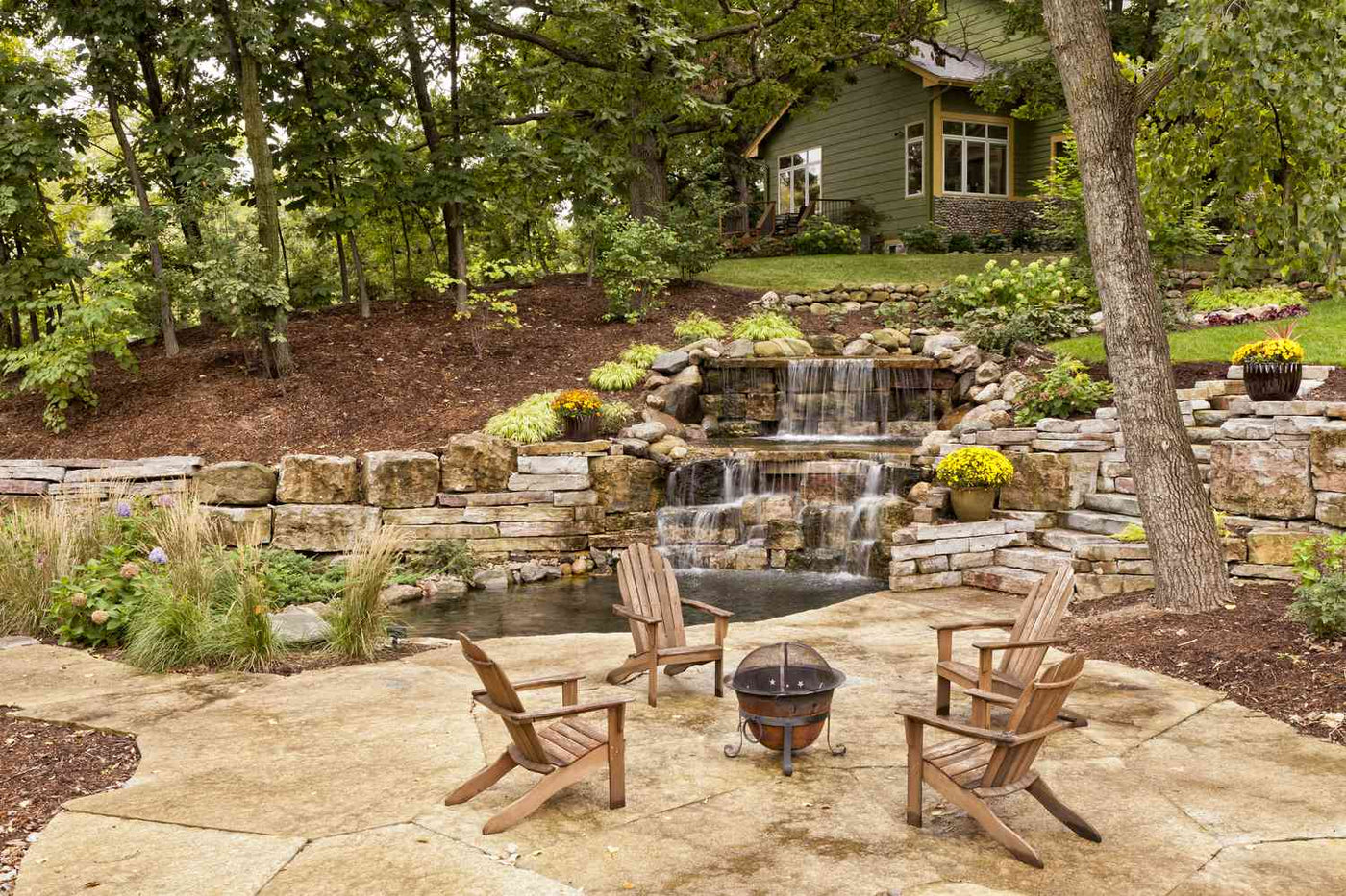 Backyard with a stone water feature, patio and planted beds after a landscape installation