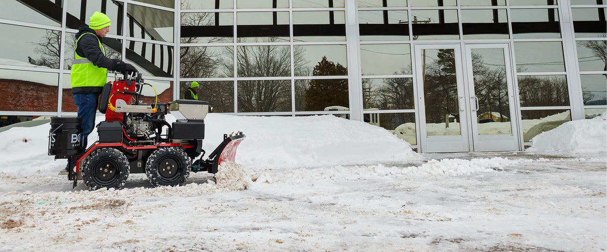 Utility vehicle with a plow clearing the entrance of a commercial building
