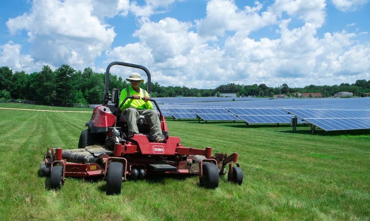 Zero-turn mower cutting a wide open lawn under a summer sky