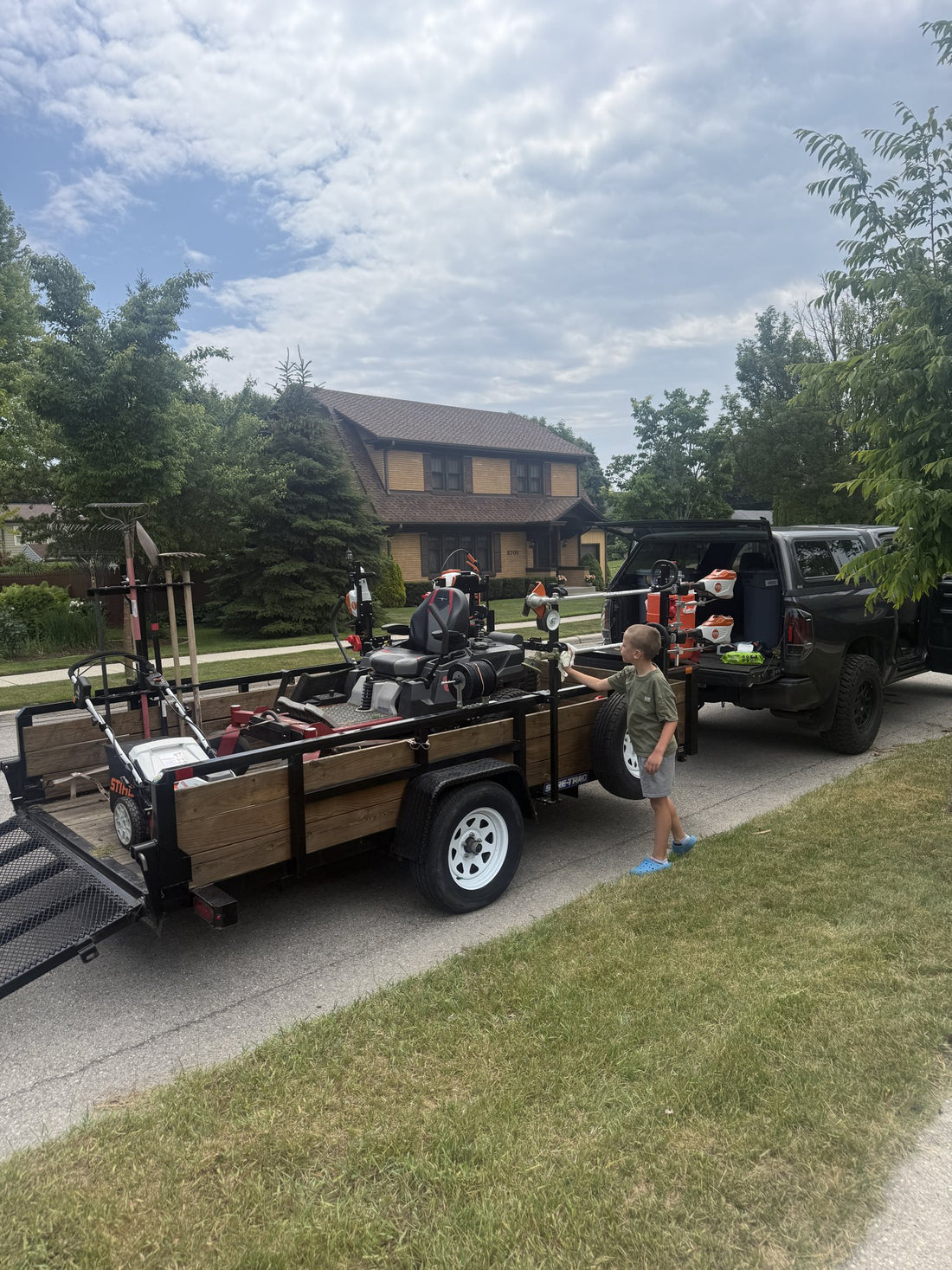 The same trailer today, loaded with the zero-turn, STIHL trimmers and blowers behind the truck, Mack wiping down the rack