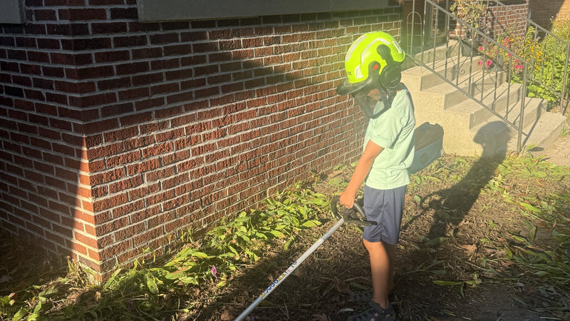 Mack cutting back perennials along a brick foundation with a string trimmer